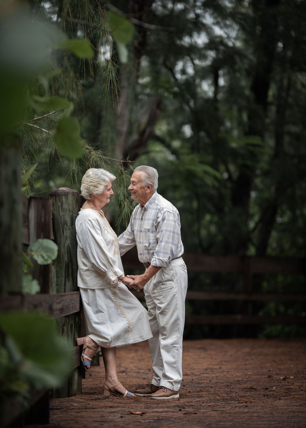 A romantic embrace on a wooden bridge surrounded by green forest.