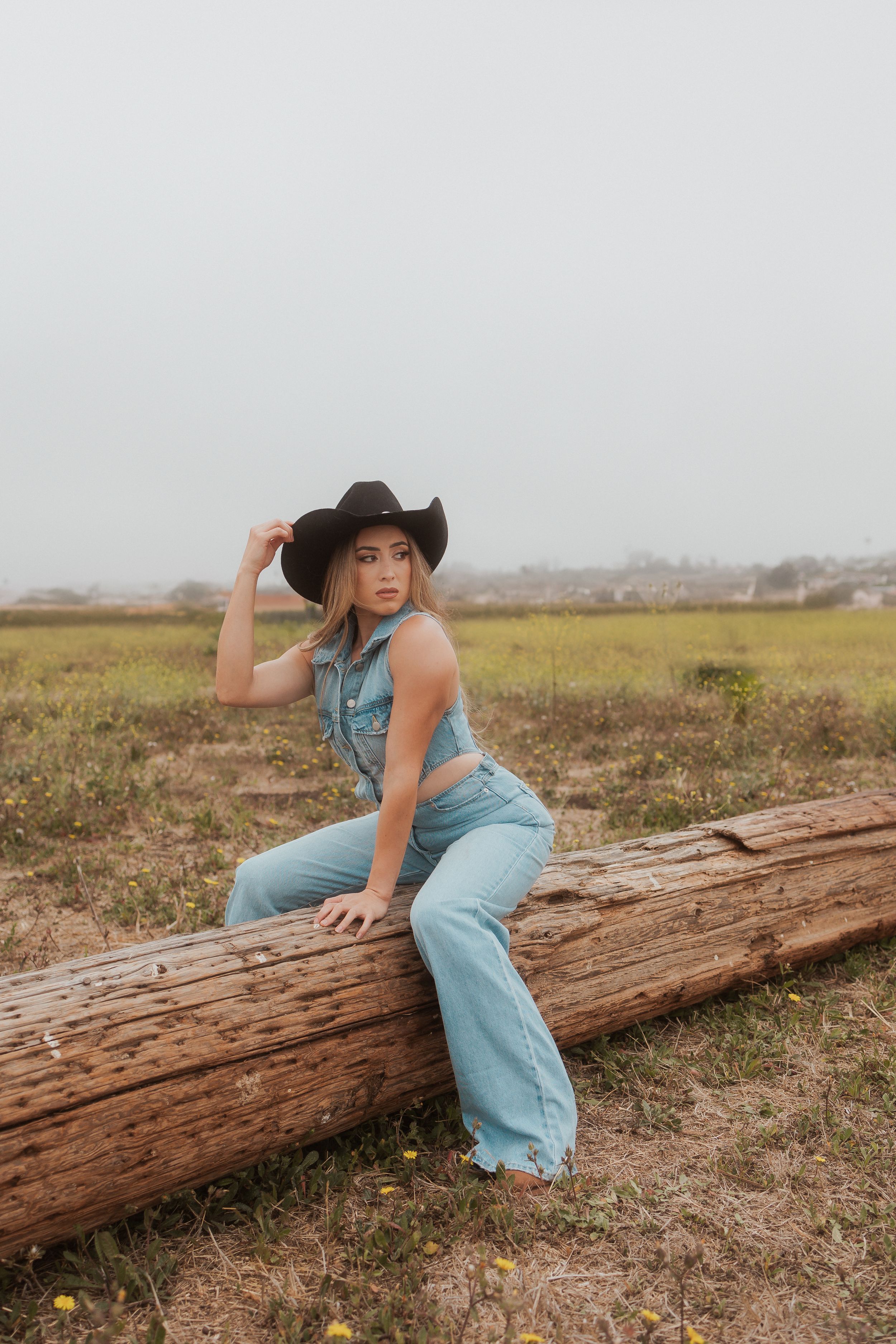 Playful western themed portrait on log wearing denim overalls and cowboy hat.