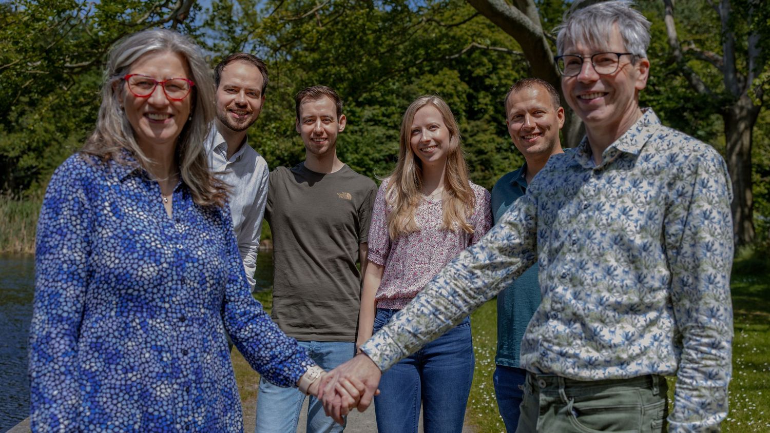 A casual outdoor group photo with six people standing by a lake.