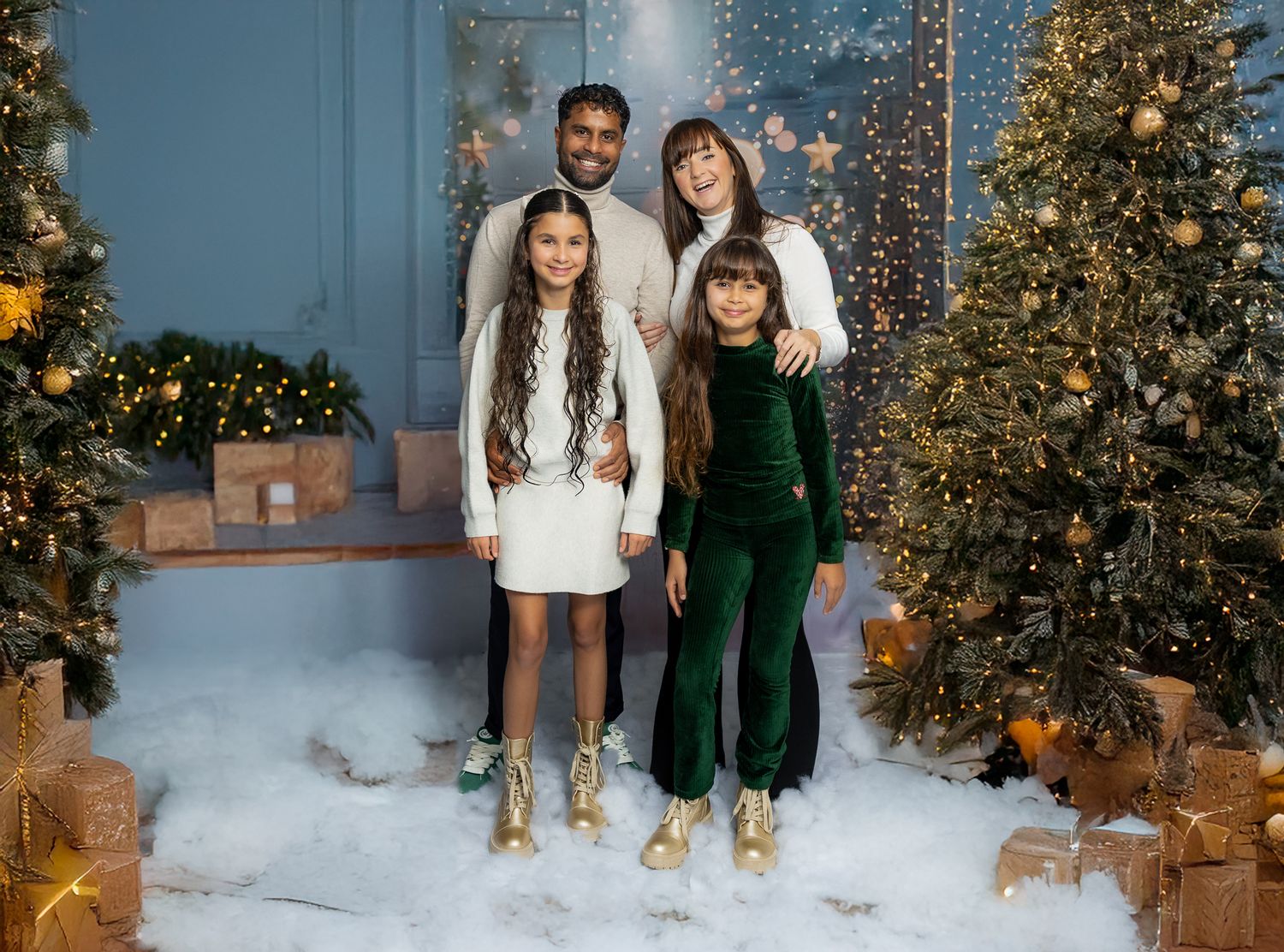 Holiday portrait with festive Christmas decor featuring decorated trees, snow, twinkle lights and cozy winter outfits.