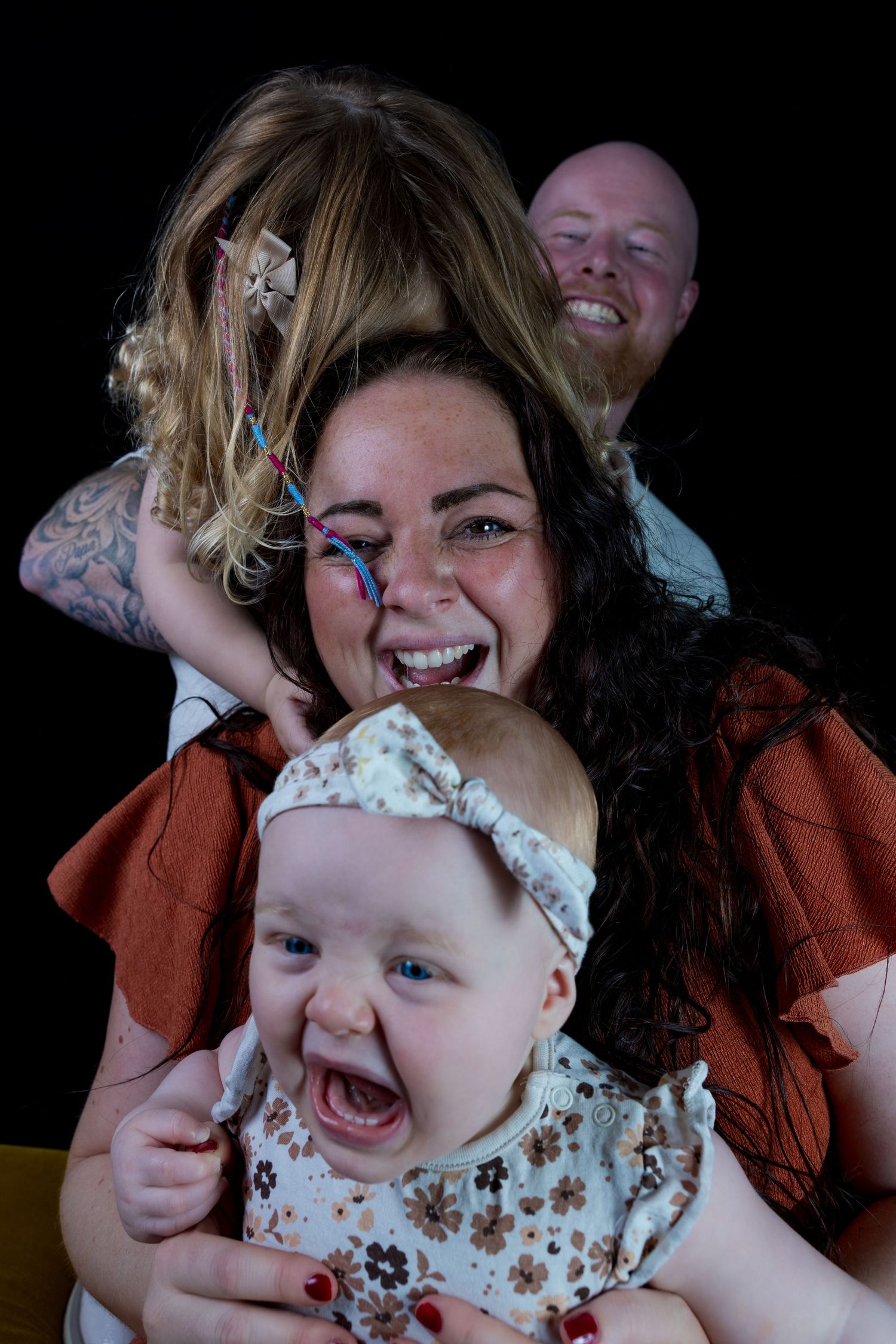 Family portrait with colorful face paint and joyful expressions against black background.

- BU Photography -