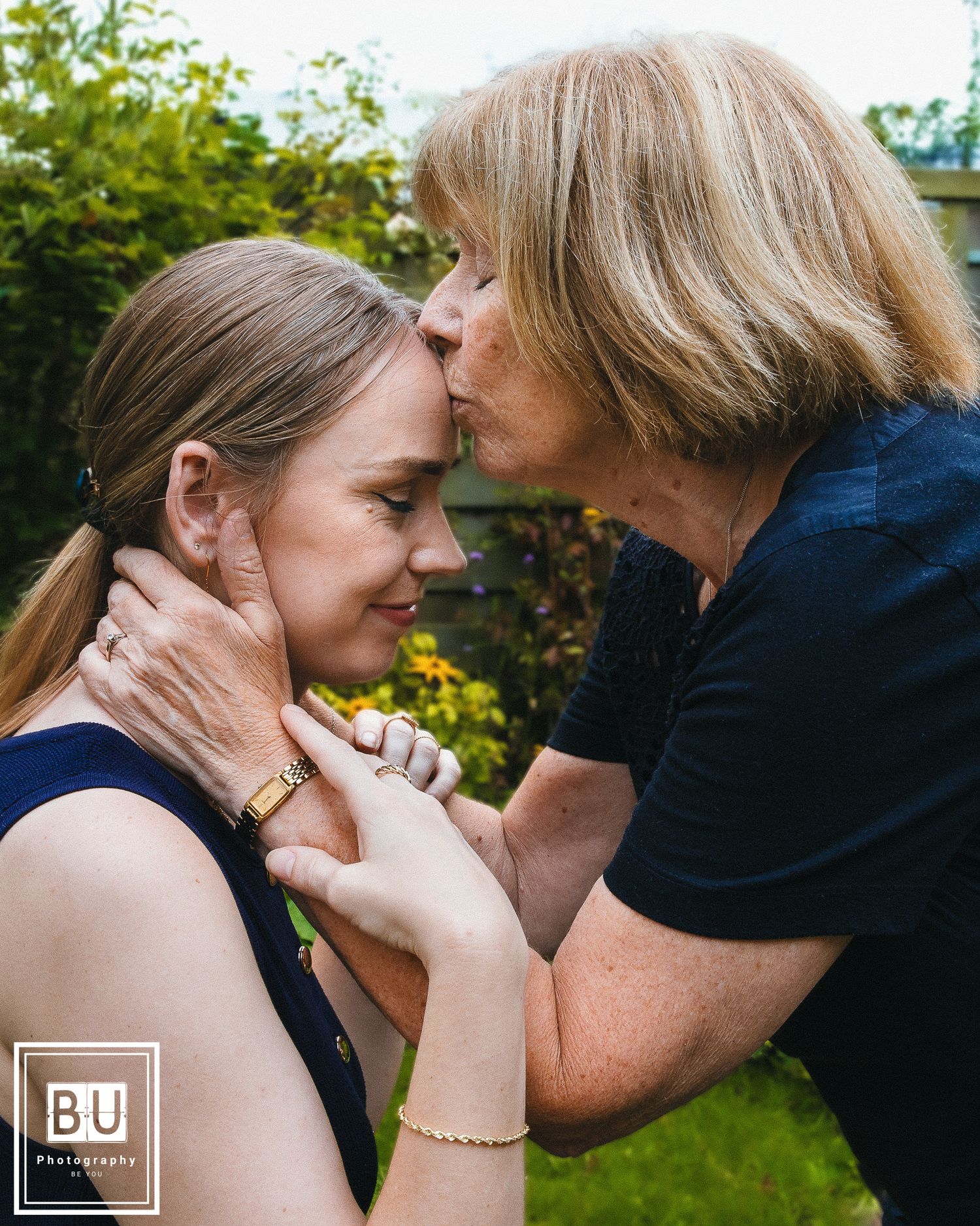 A tender moment captured outdoors showing affection and care between two people in navy blue clothing.

- BU Photography -