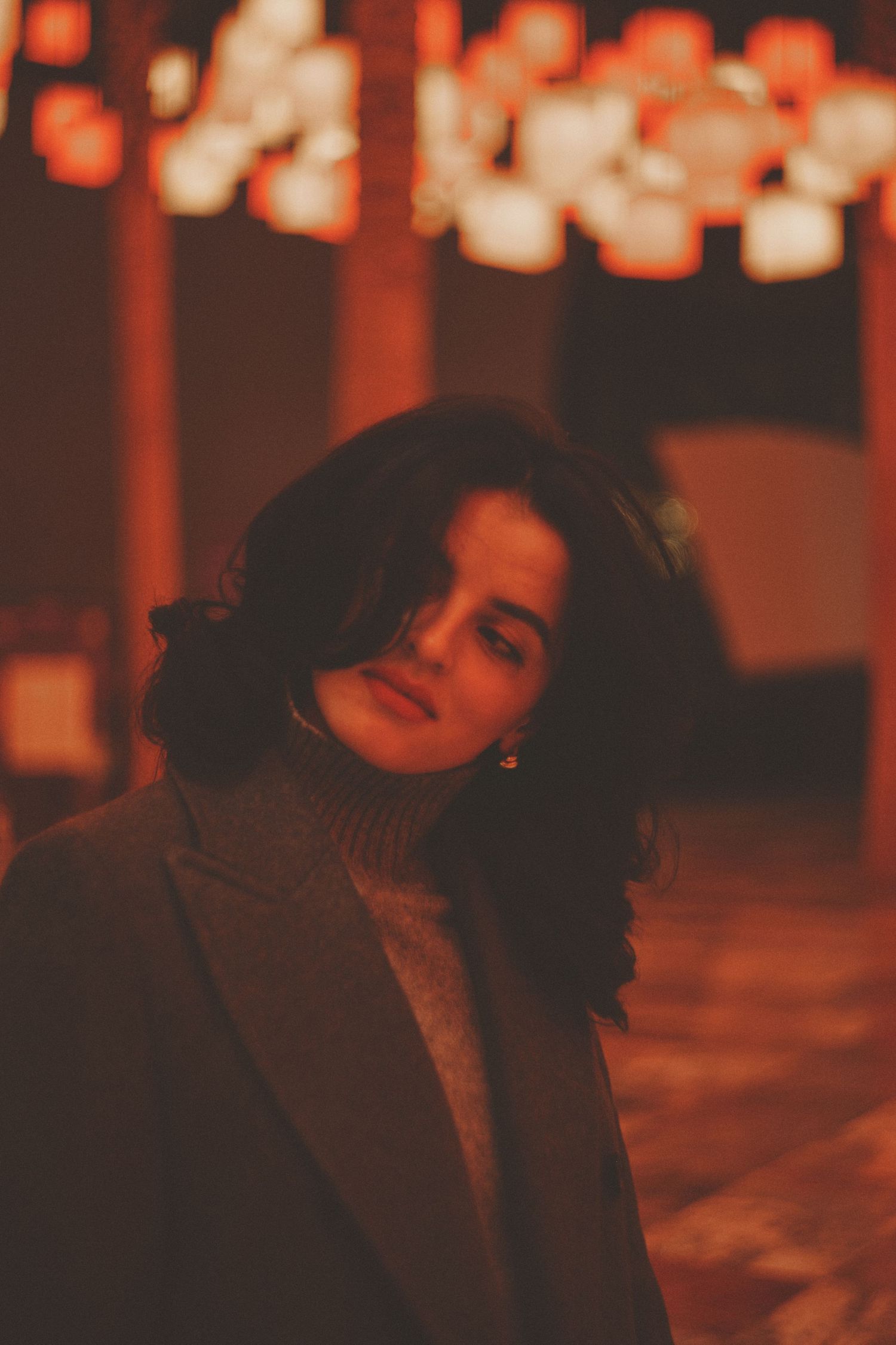 Moody portrait in warm lighting with bokeh lanterns in background.
