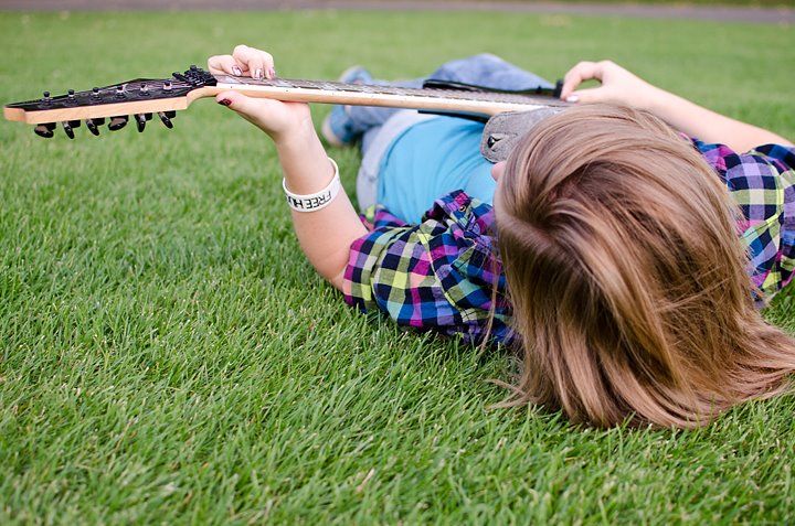 A person lying in green grass while holding a guitar, photographed from above.