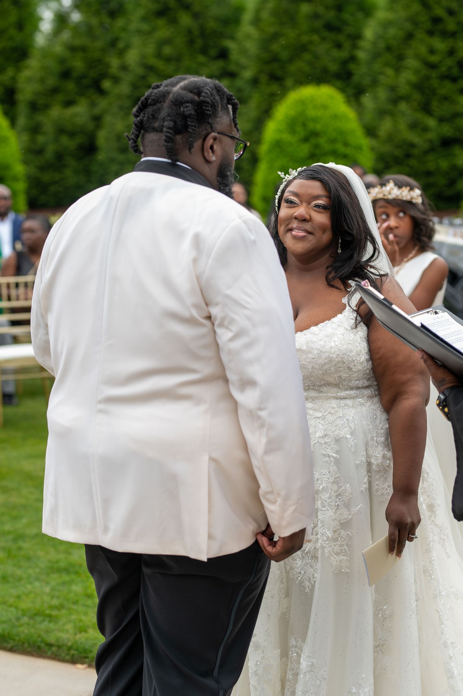 Happy couple exchanges vows during outdoor garden wedding ceremony surrounded by lush greenery.