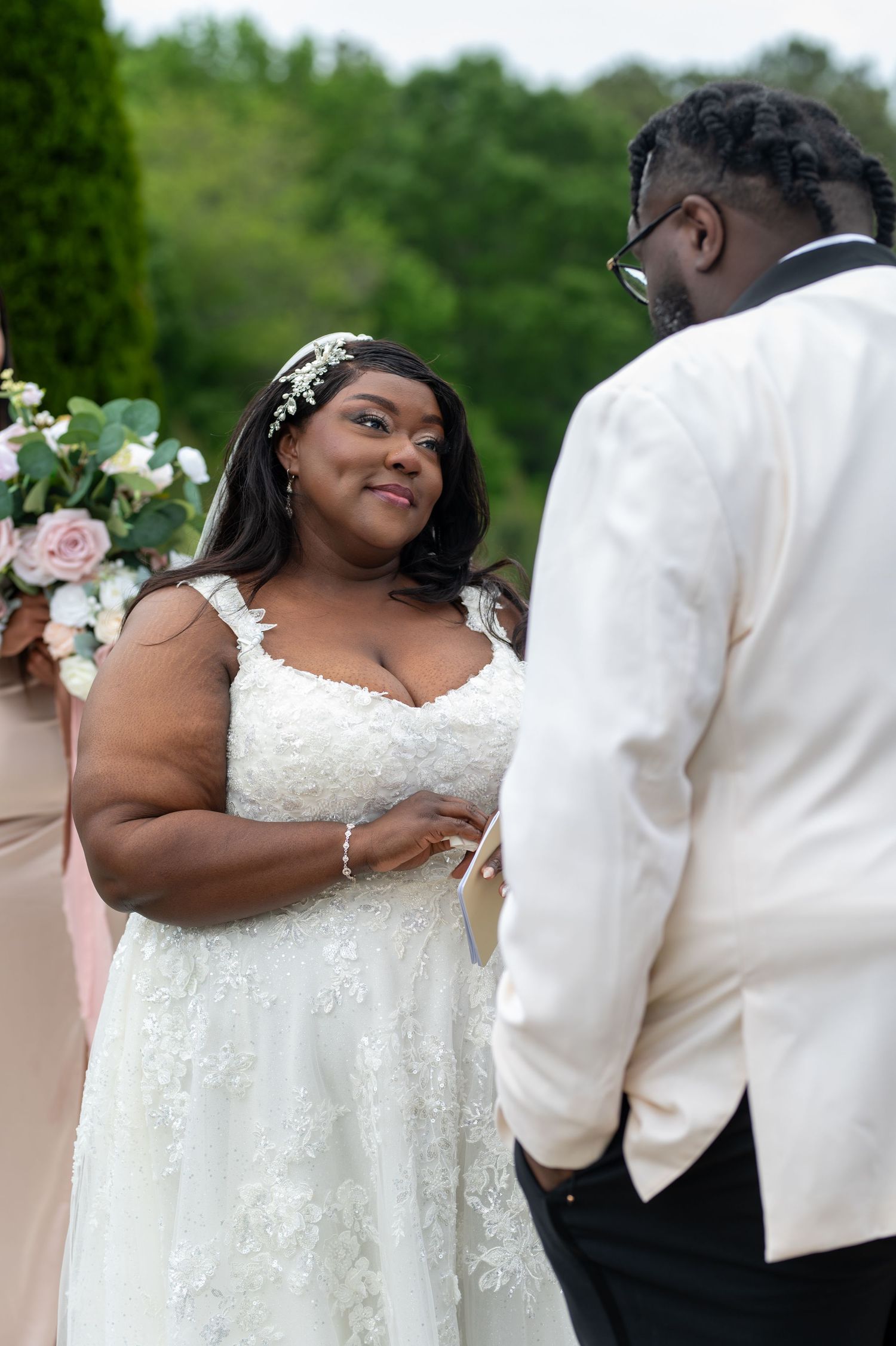 Beautiful bride in lace wedding gown shares tender moment with groom during outdoor ceremony.