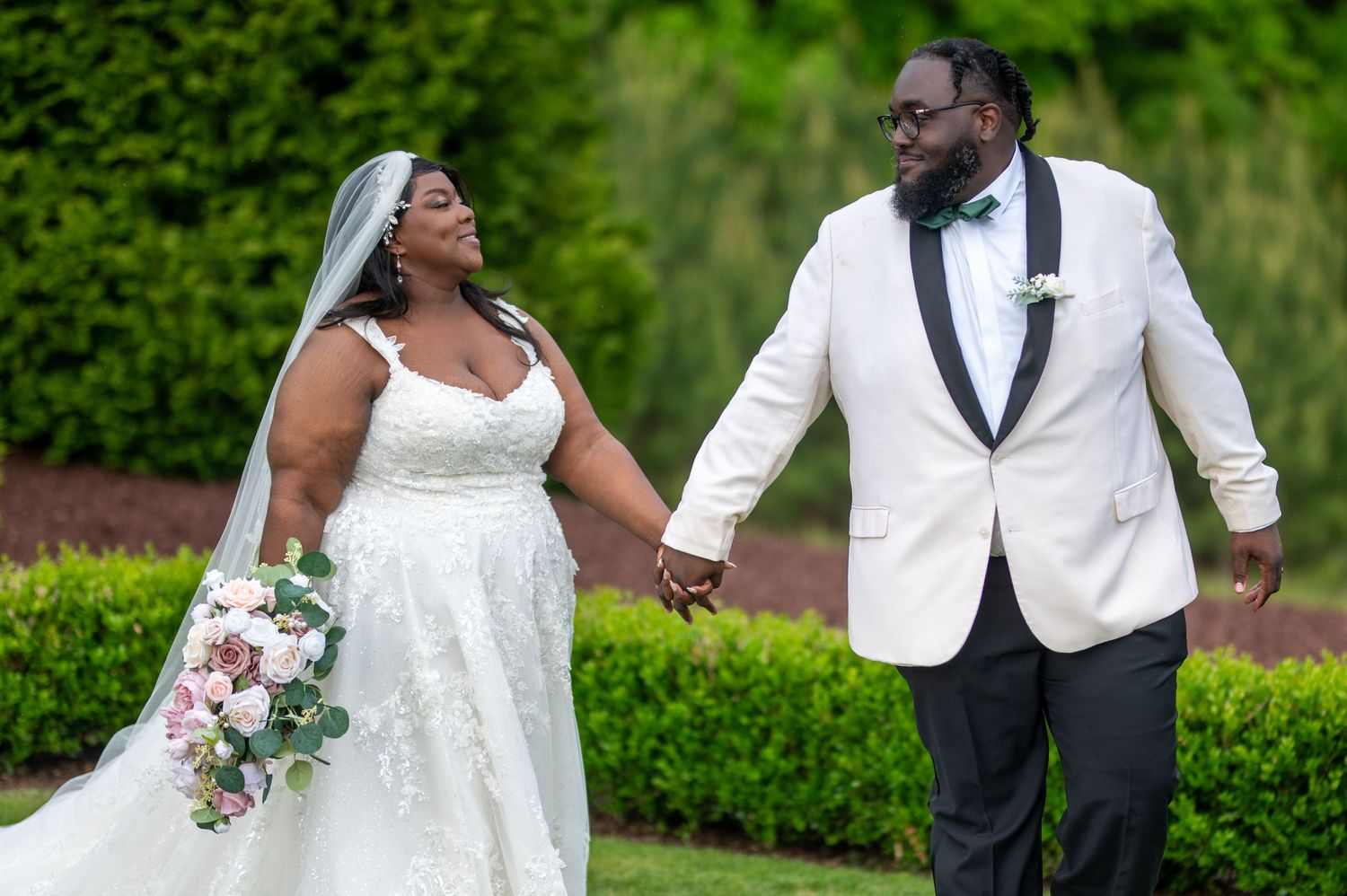 Newlyweds share loving glance while holding hands in beautiful garden setting.