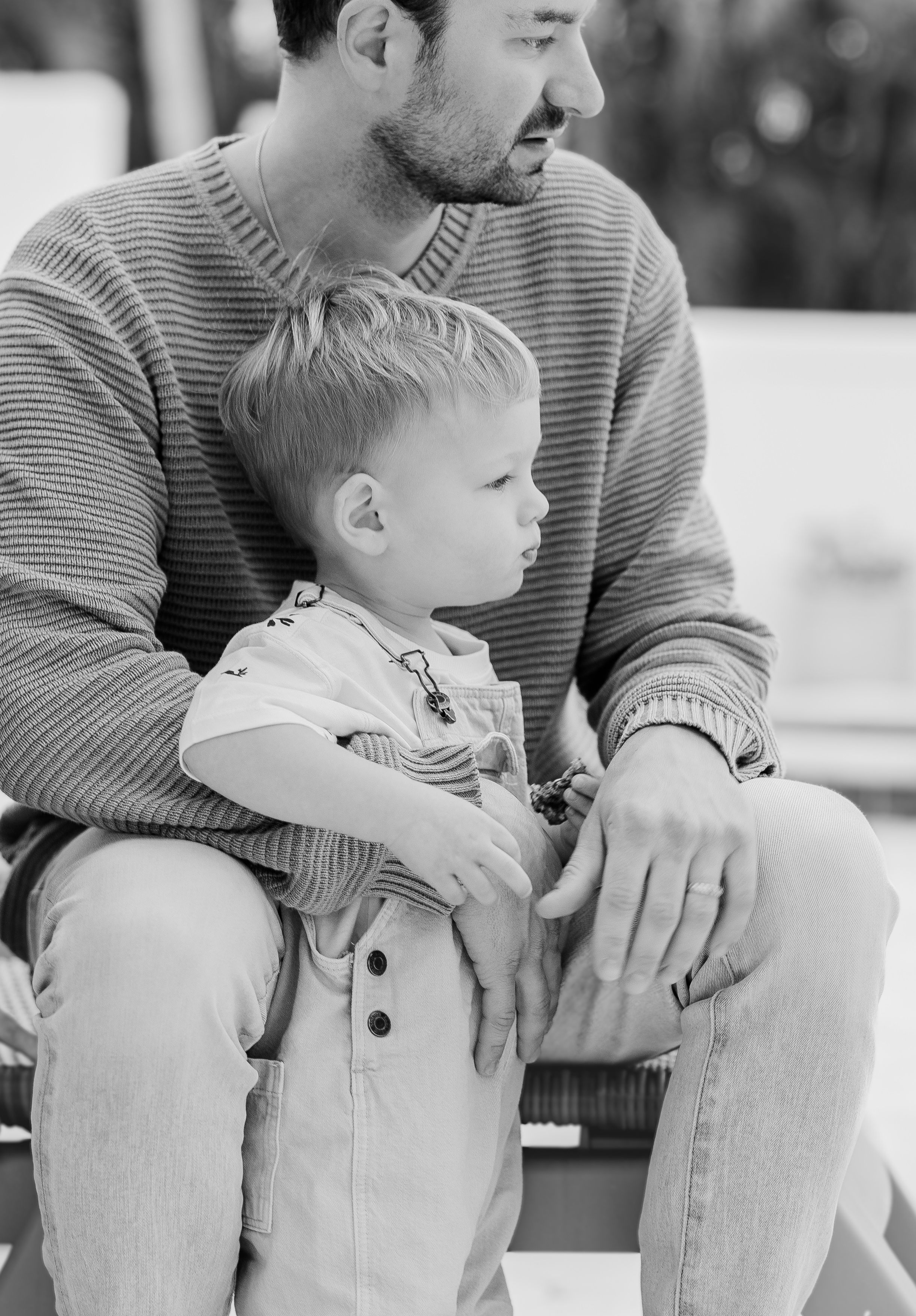 A tender moment captured in black and white as a toddler sits on someone's lap wearing overalls.