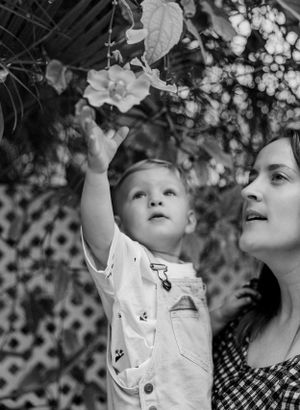 A black and white moment of wonder as a child reaches up to touch flowers while being held.