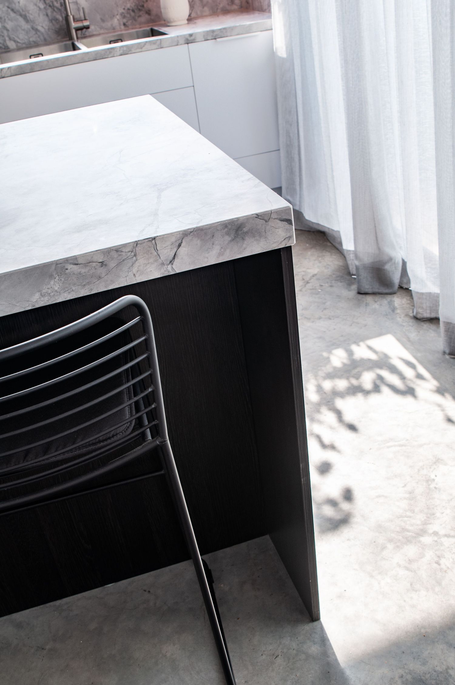 Close-up of black dining chair and marble countertop with sunlight casting shadows.