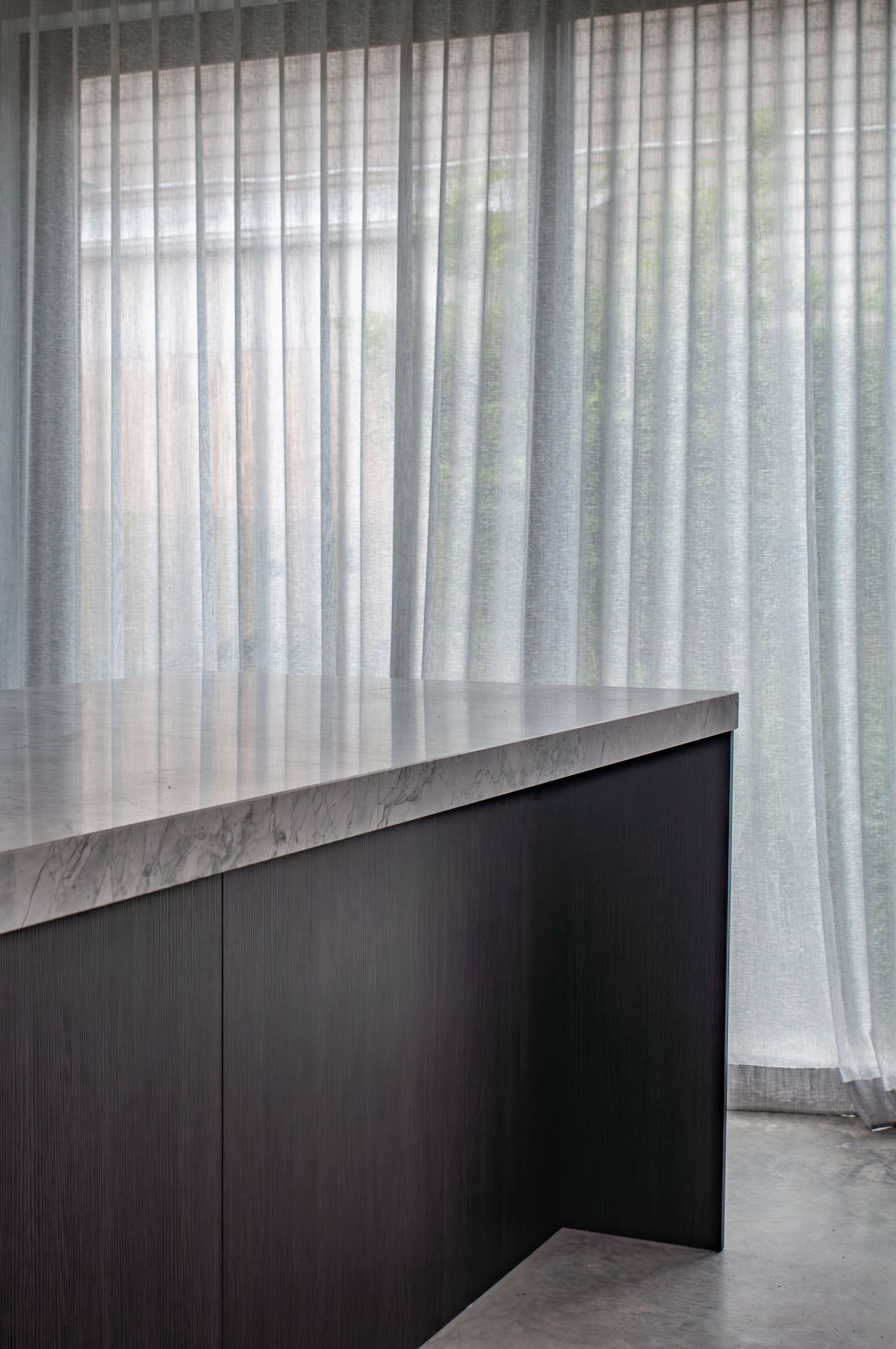 Minimalist kitchen counter with sheer white curtains and concrete floors.