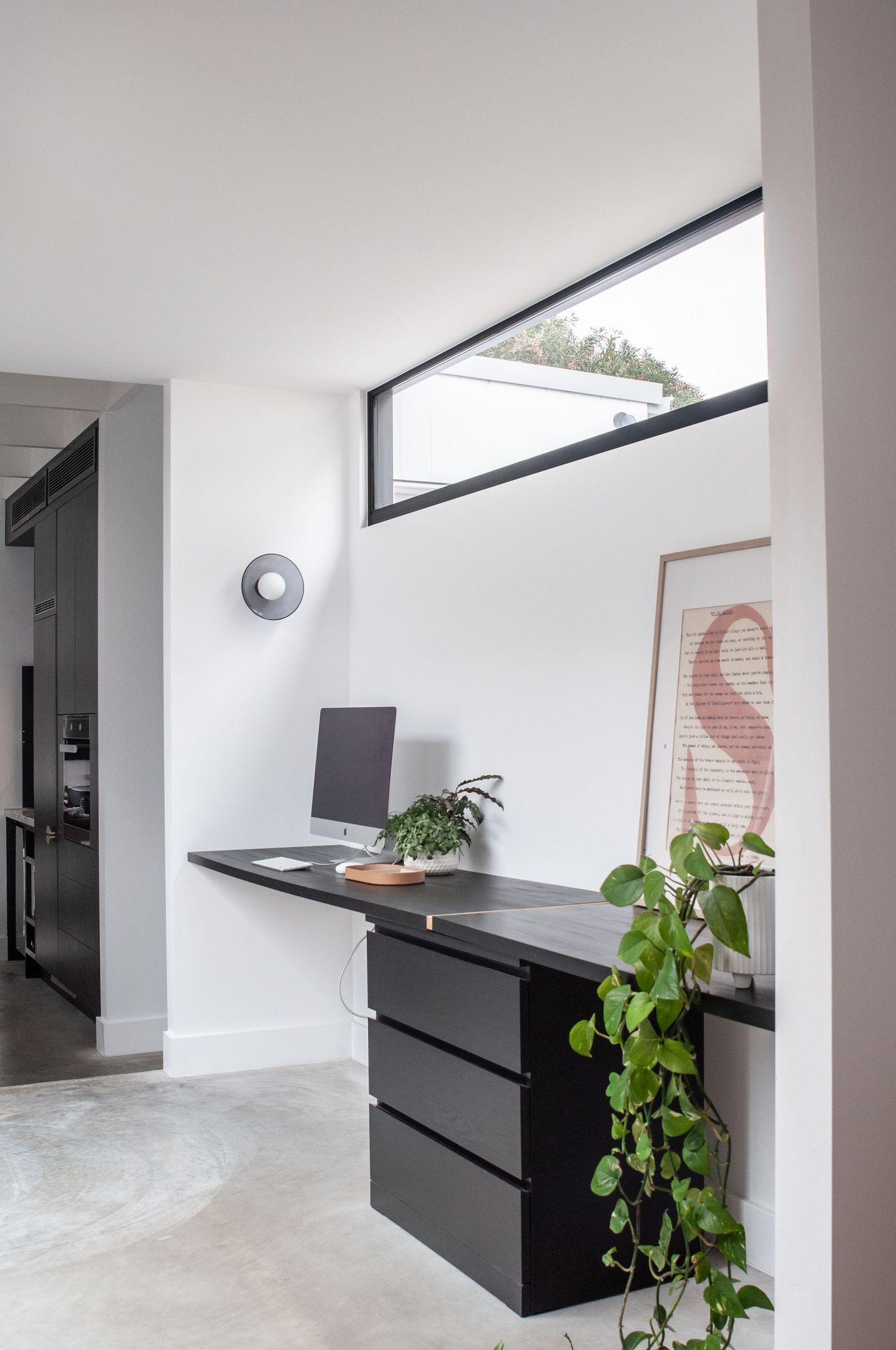 Modern home office area with black desk, trailing plants, and high window.