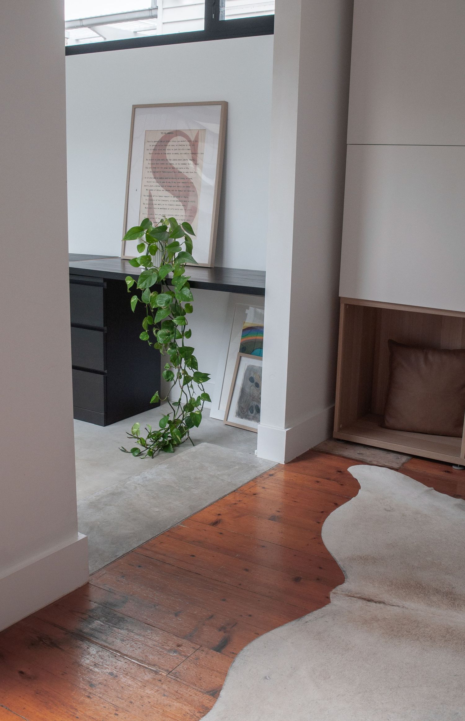 Interior space with black desk, hanging plant, and transitioning wood to concrete flooring.