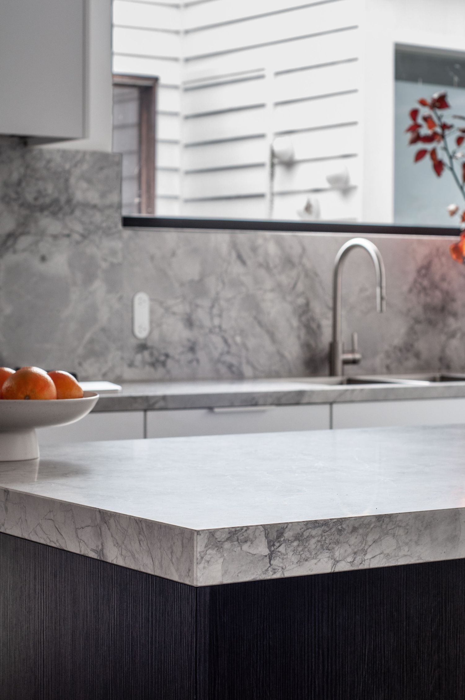 Close-up of marble kitchen countertop and backsplash with bowl of oranges.