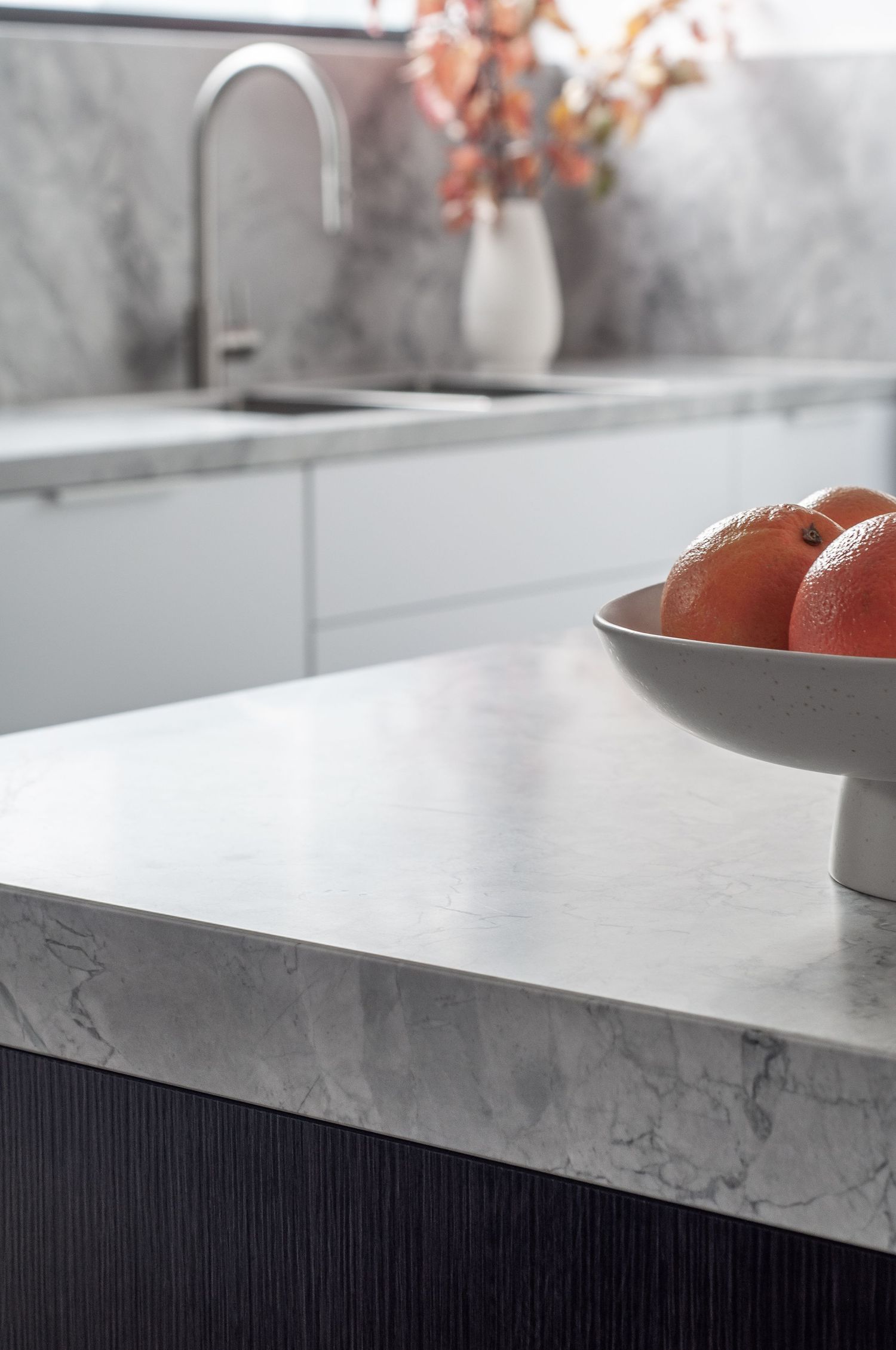 Modern kitchen counter with white marble top, chrome faucet, and a bowl of fresh tomatoes.