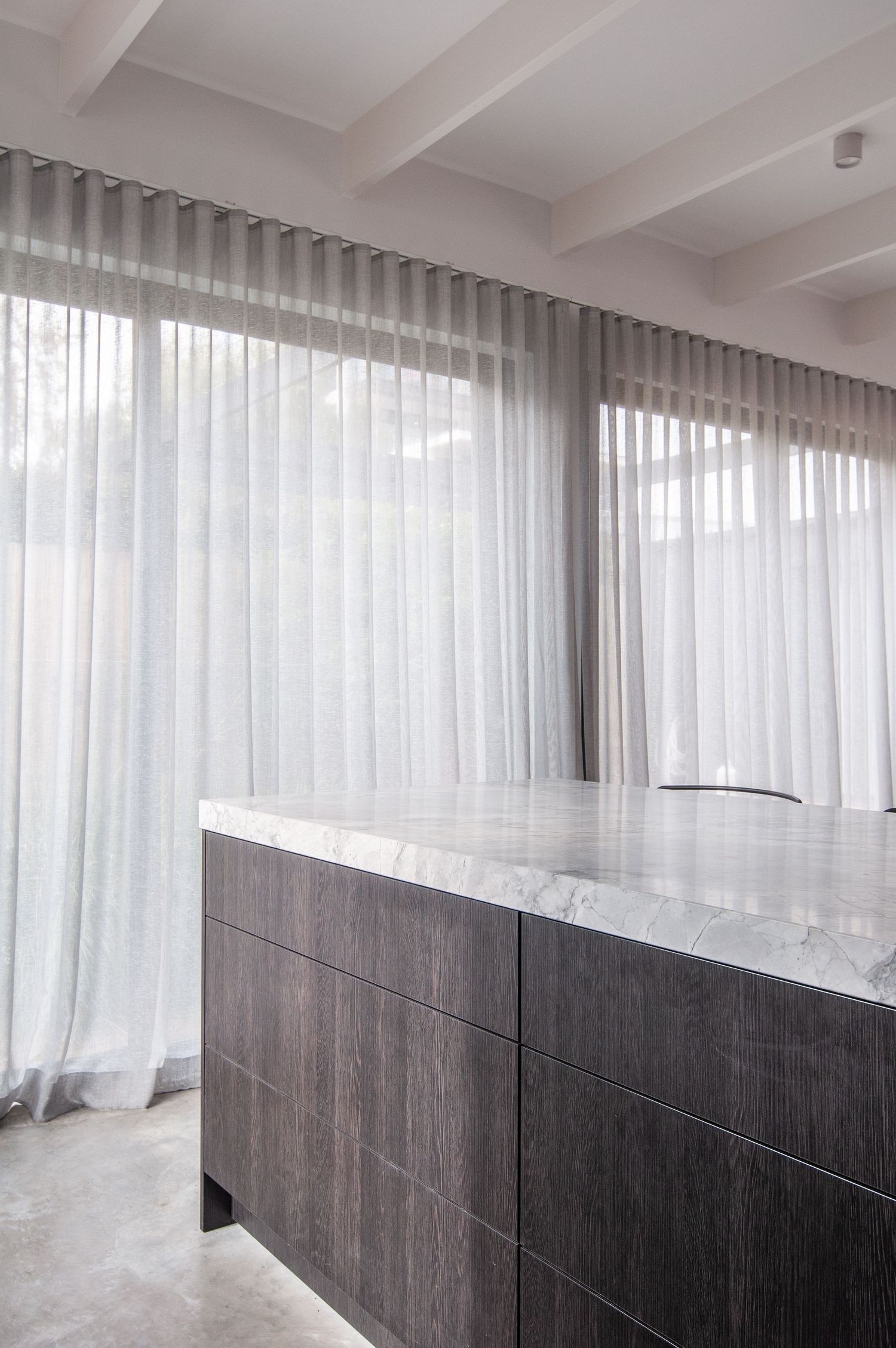 Minimalist interior with floor-to-ceiling sheer curtains and dark wood cabinetry with marble countertop.