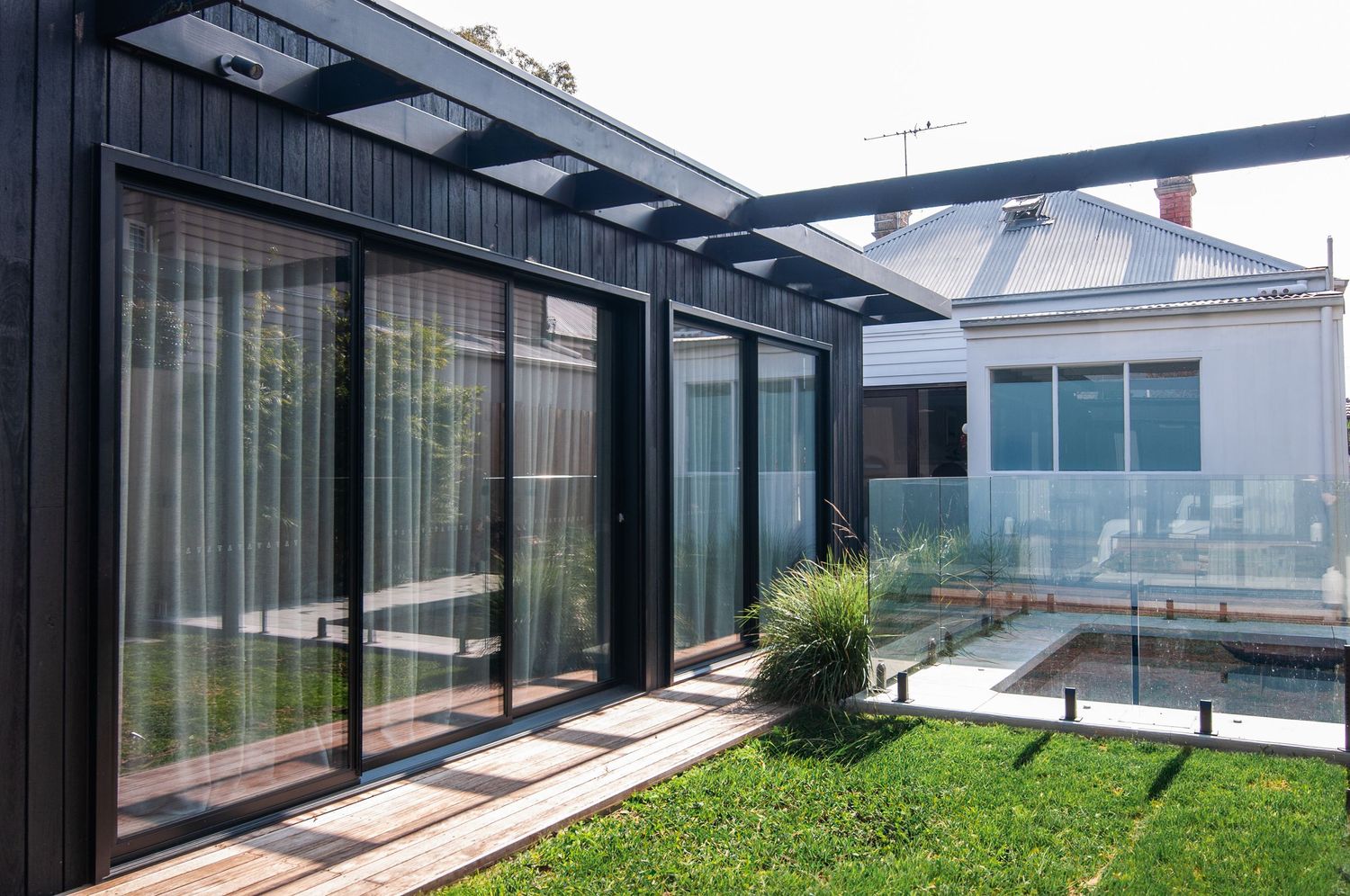 Modern black-framed glass house extension with sliding doors opening to a landscaped garden.