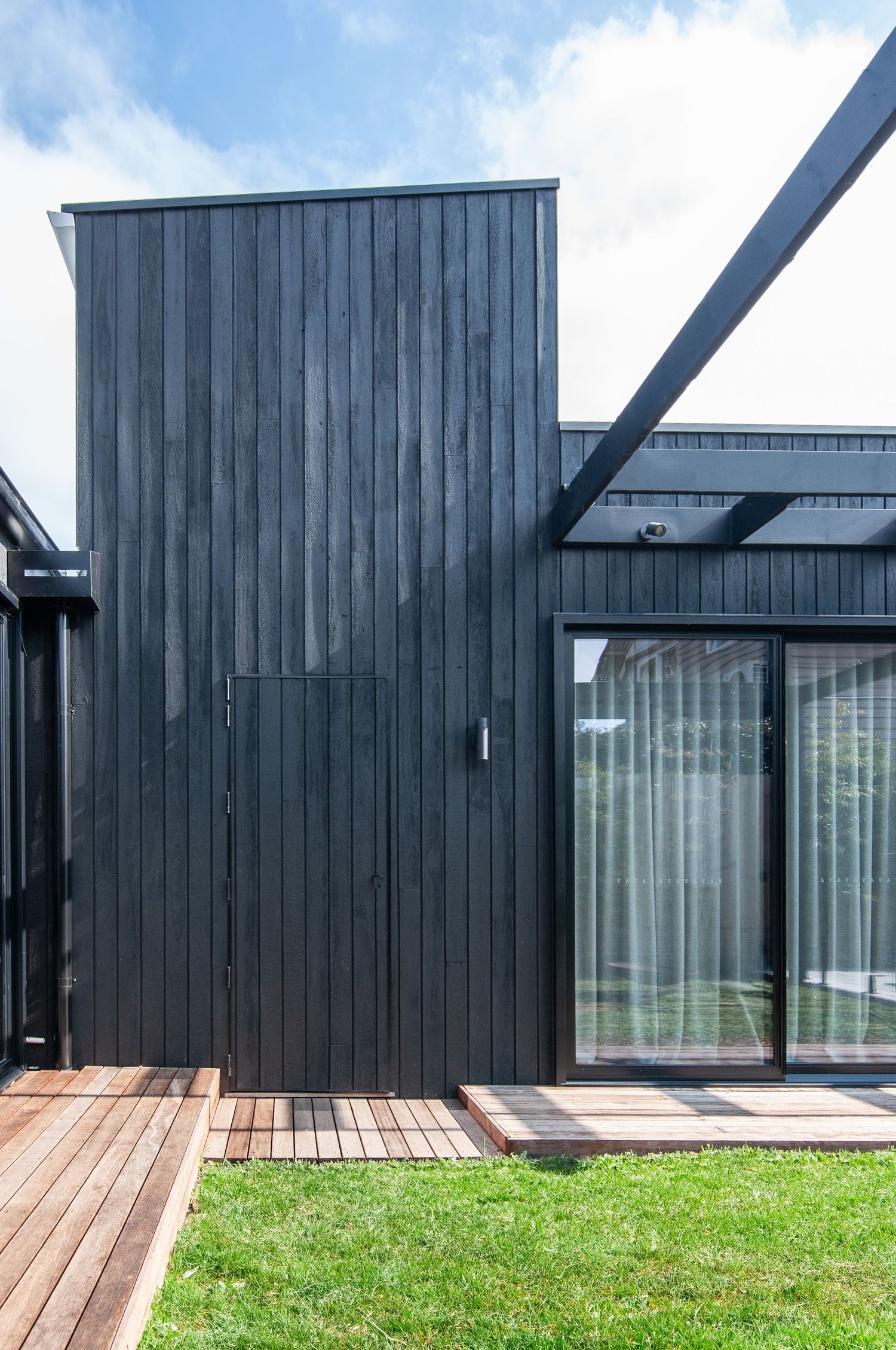 Contemporary black wood-clad house exterior with glass sliding doors and wooden deck.