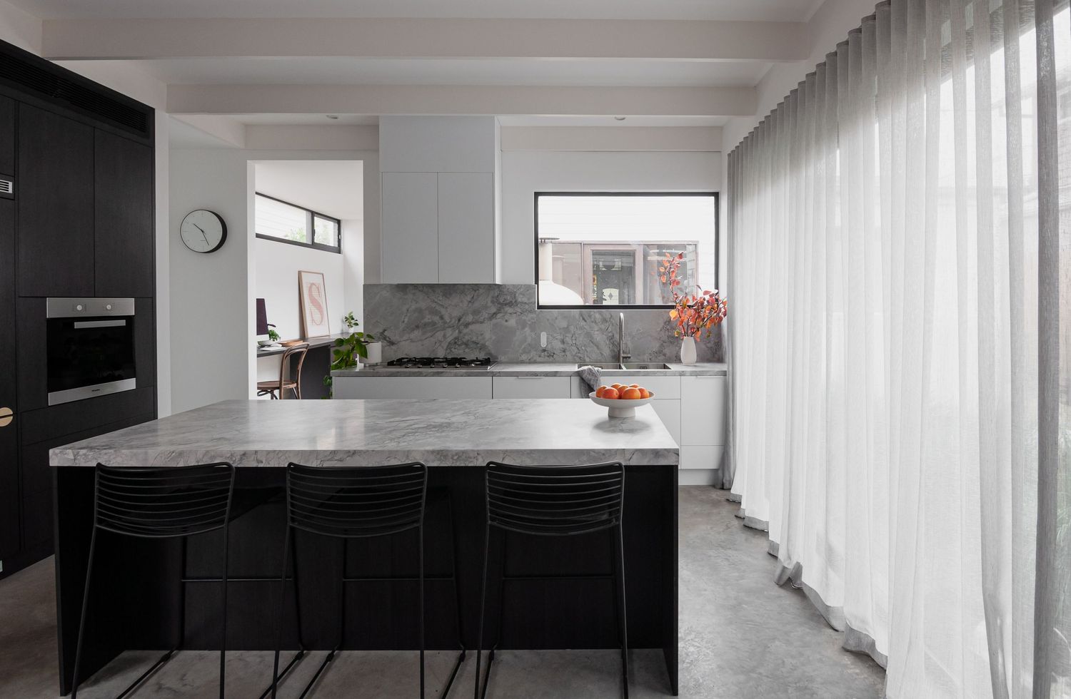Contemporary kitchen with black and white contrast, marble countertops, and floor-to-ceiling curtains.