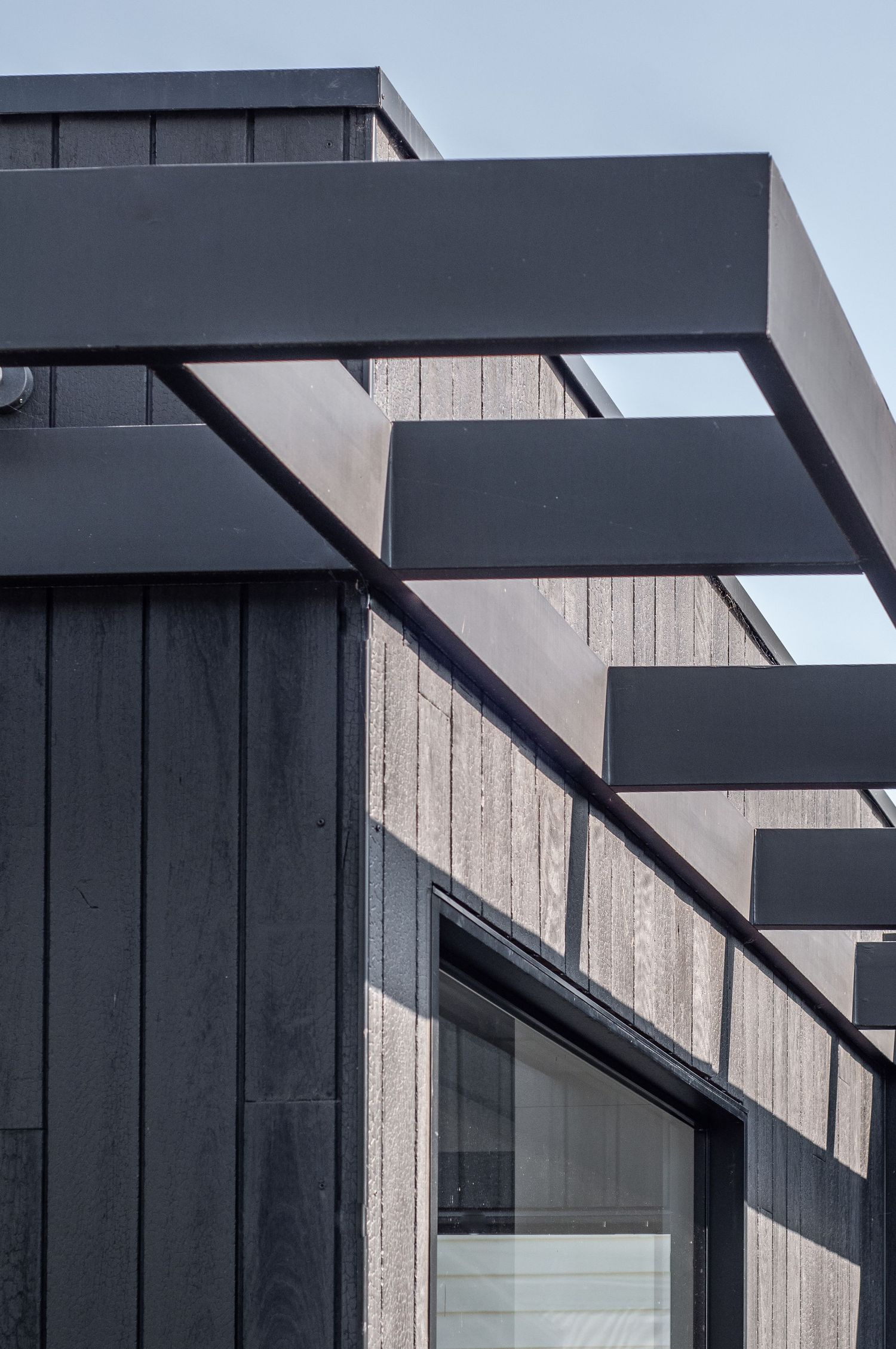 Modern black architectural detail showing cantilevered roof elements against wood siding.