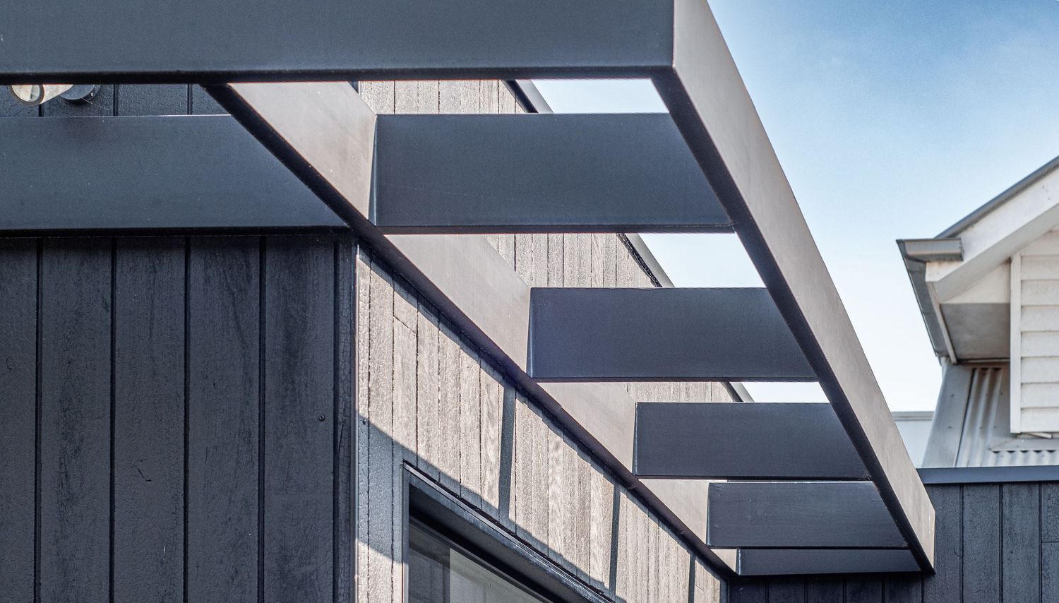 Geometric black metal overhangs create striking shadows on contemporary wood-clad building exterior.
