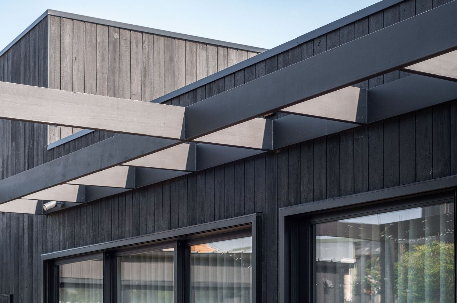 Series of parallel metal beams extend from dark wood-clad exterior wall creating architectural rhythm.