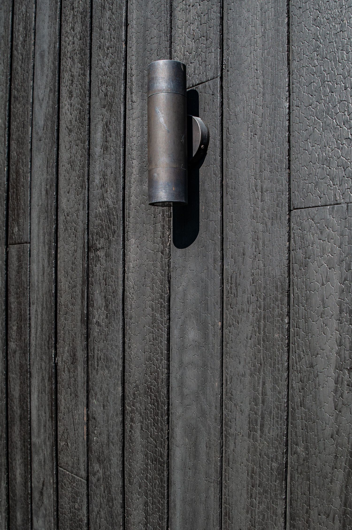 Cylindrical outdoor wall light mounted on vertical black wood siding.