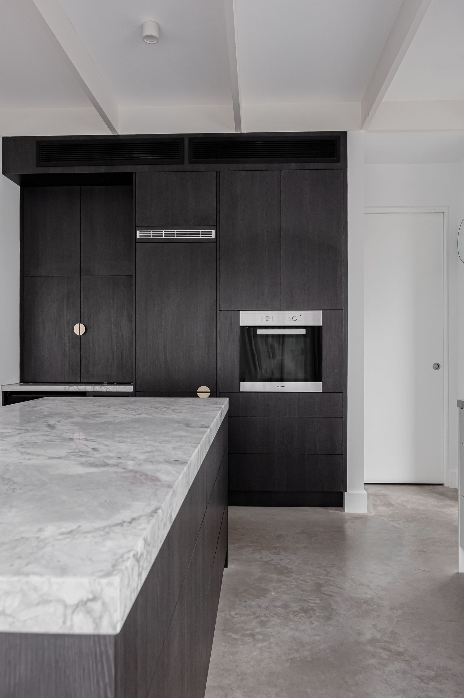 Sleek black kitchen cabinetry with built-in oven and marble countertop island.