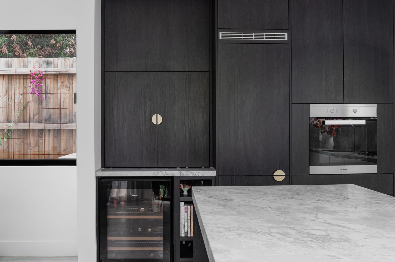 Black kitchen cabinets with marble countertop and wine fridge in contemporary style.