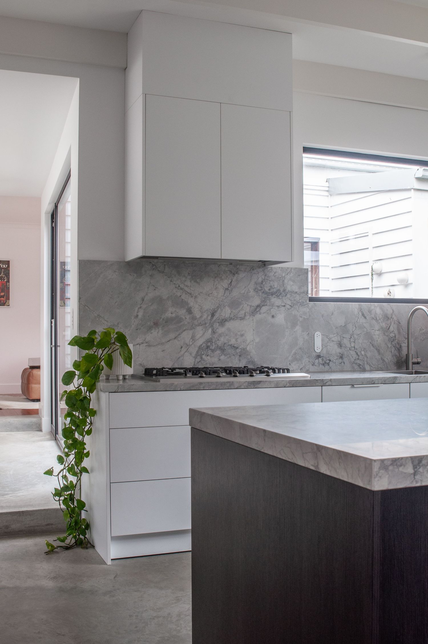 Modern white kitchen with marble backsplash, dark island, and trailing plant.