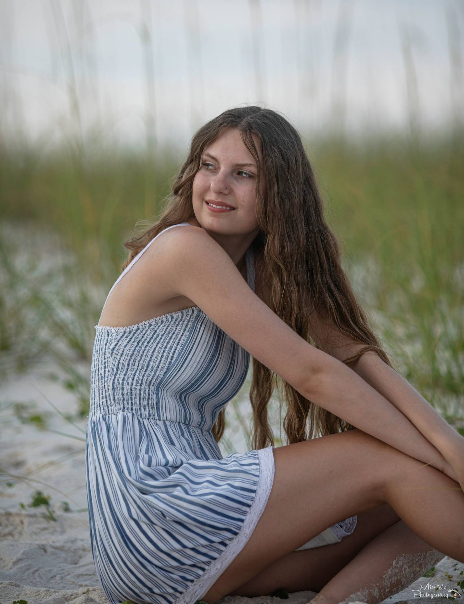 Young woman in striped summer dress sitting on sandy beach.