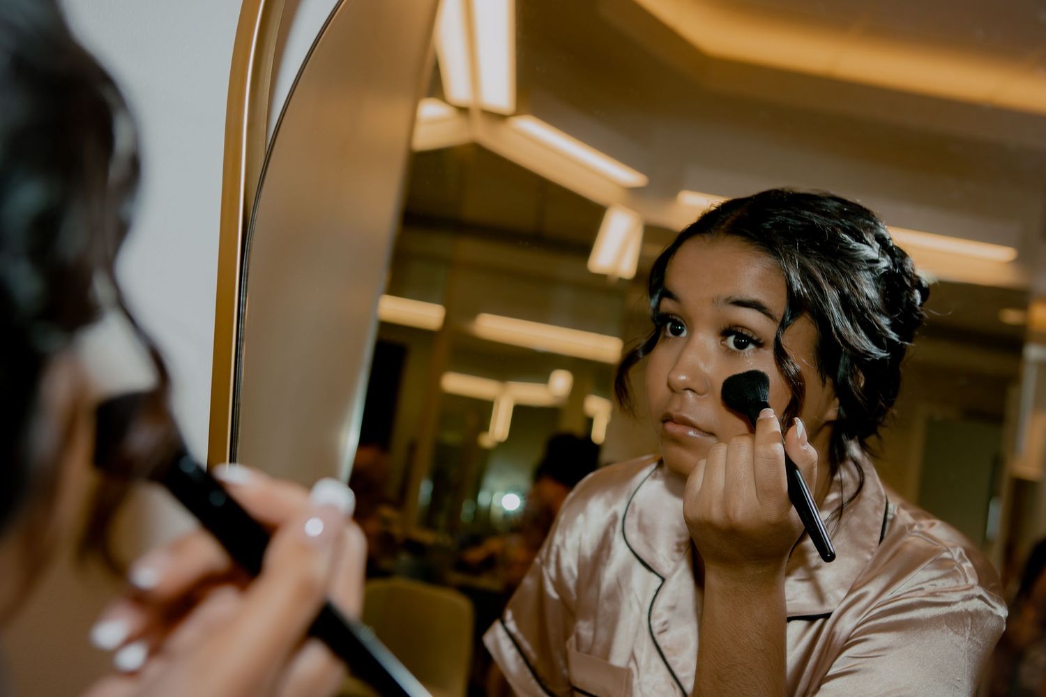 Person applying makeup in front of mirror during wedding preparations.