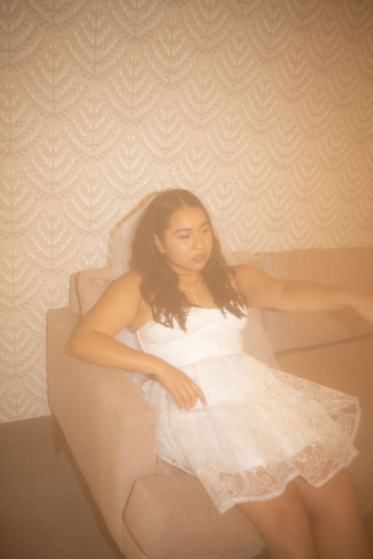 A dreamy sepia-toned photo shows someone in a white lace dress reclining on a beige armchair.