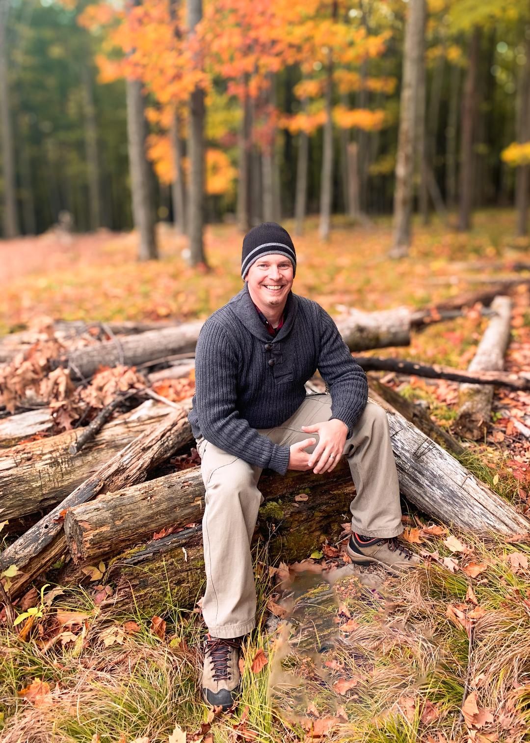 Photography of young man sitting on a log in nature, surrounded by fall leaves and colors.  Blue Onion Photography.