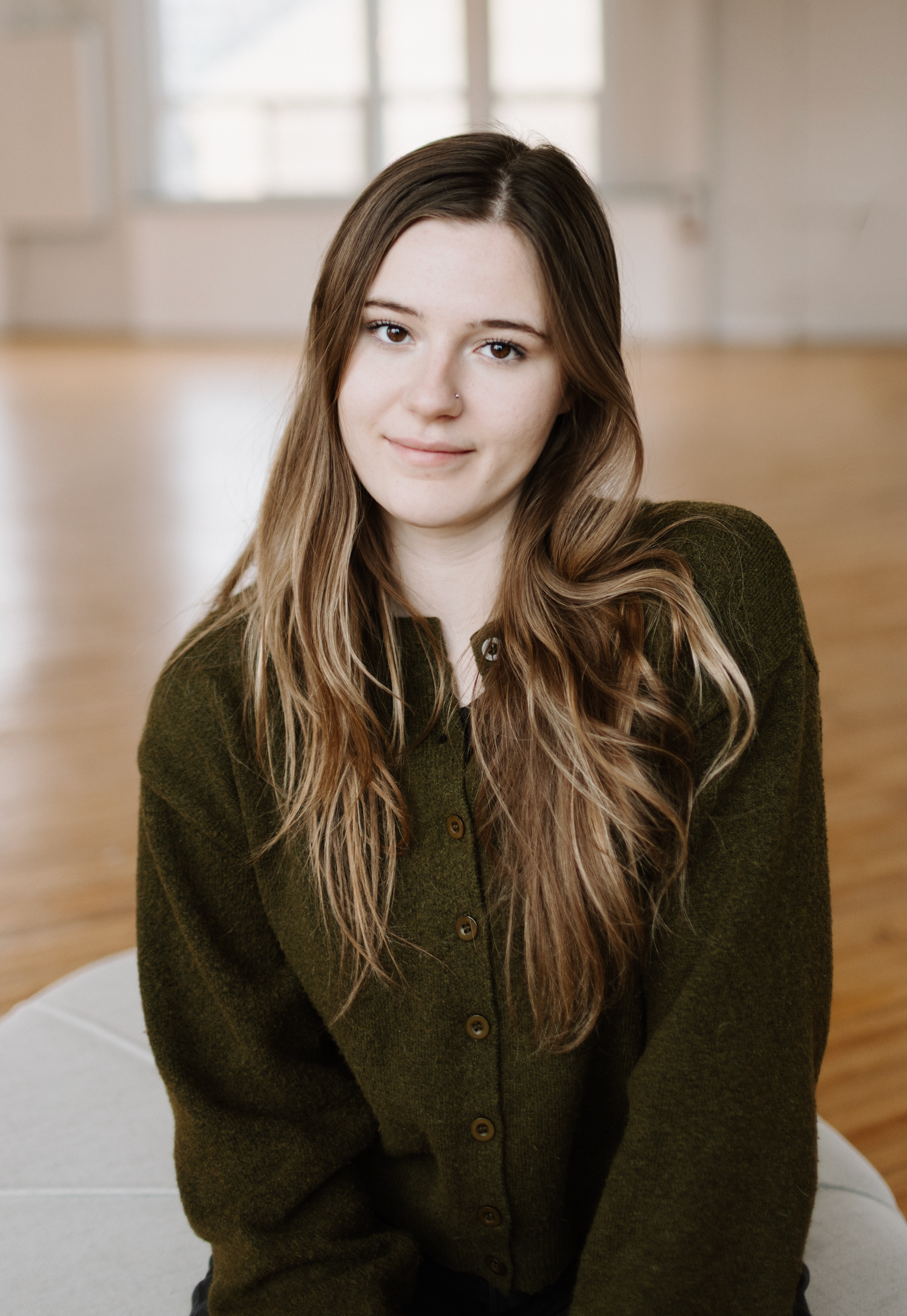 Professional studio portraits showing warm expressions against a light wooden floor background in dark sweater.