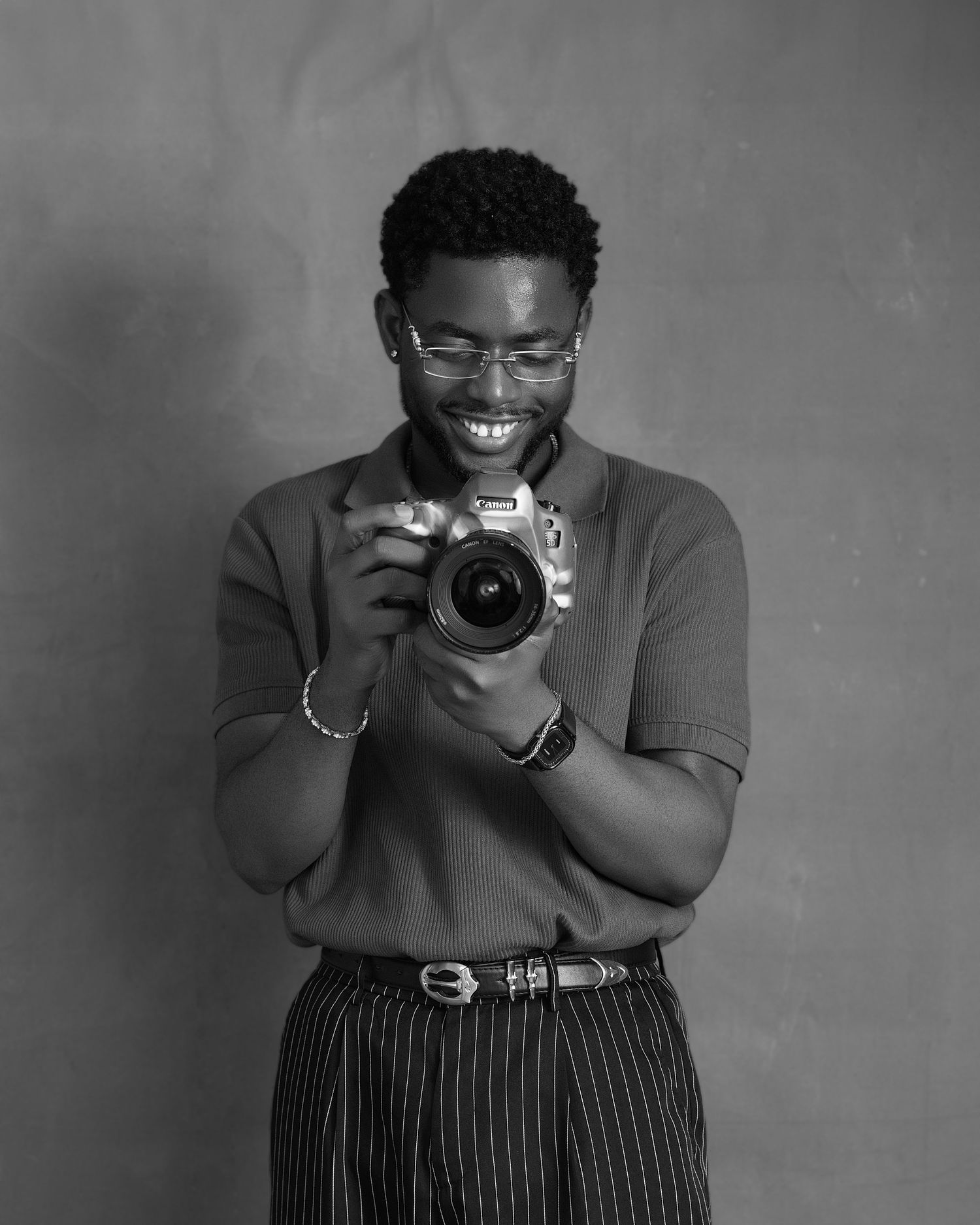 Timi Olumide wearing a navy quarter-zip sweater smiles while holding lenses against a bright blue background.