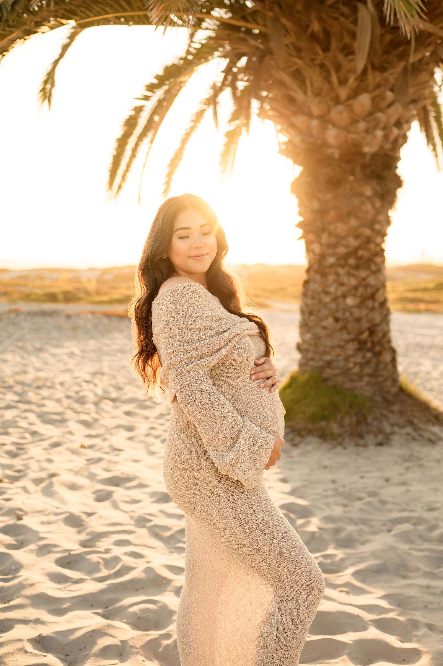 woman in Meshki see through crochet dress holds pregnant belly during her sunset beach photoshoot by Ventura and Santa Barbara Photographer