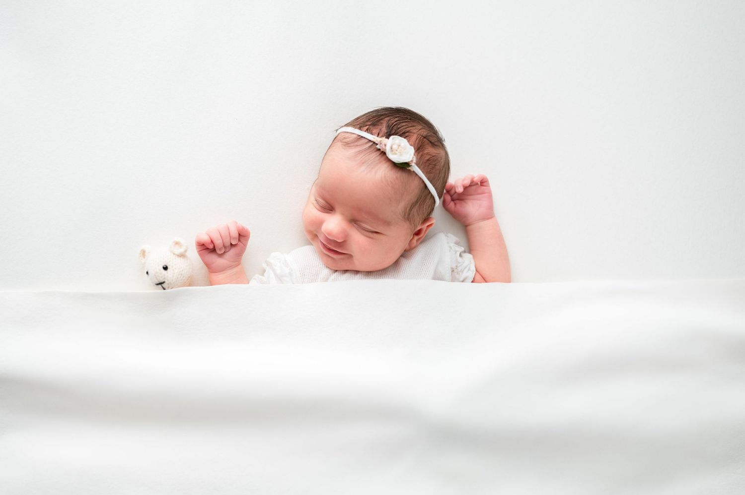 Baby girl smiling while swaddled in soft white fabric at Woodbury MN luxury photography studio