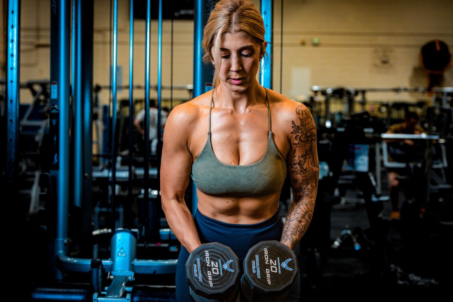 Athletic figure holding dumbbells during workout in a dimly lit gym setting.