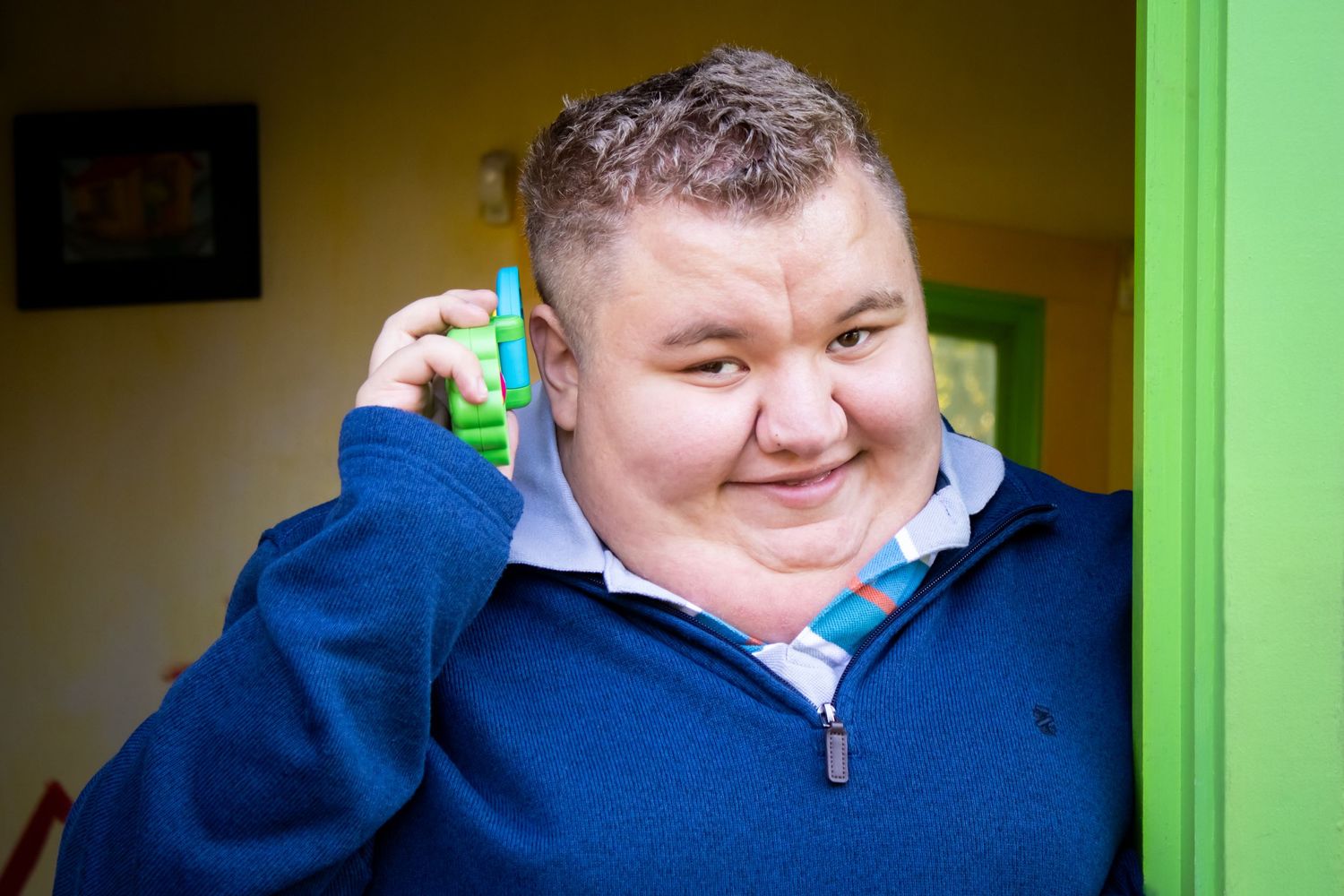 Playful boy holding a toy phone up to his ear pretending to be talking on it while sharing a subtle smile.
