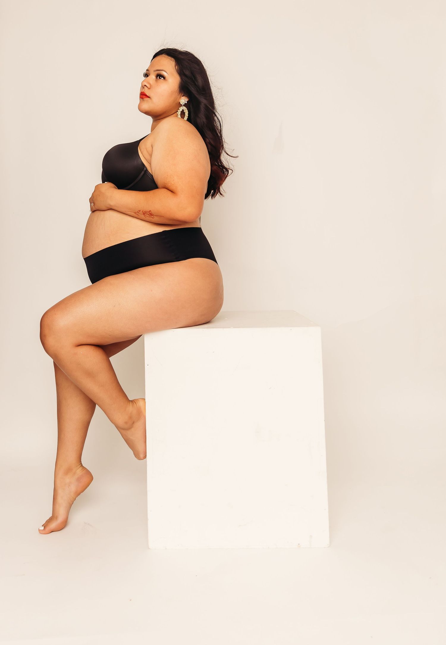 Artistic portrait of woman in black lingerie posed on white cube.