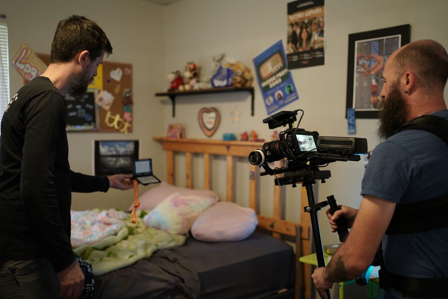 Camera operator filming in bedroom with stuffed animals and posters visible.