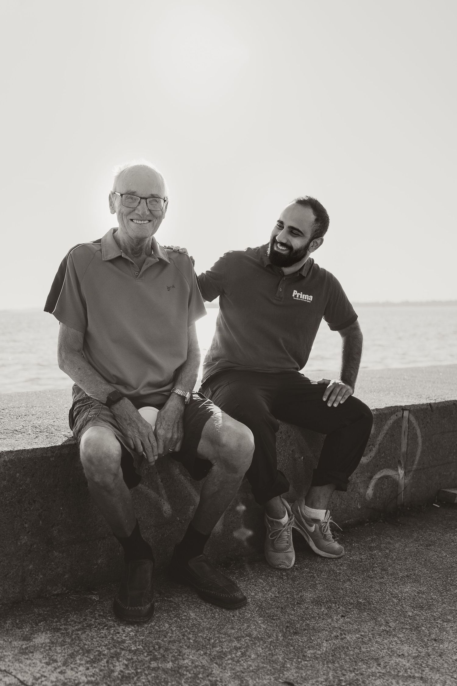 A black and white photo of two people sitting together by the ocean.