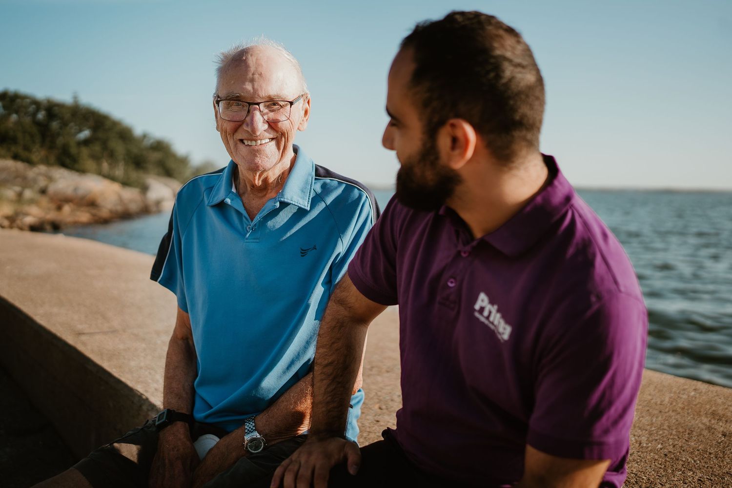 Two people share a joyful conversation while sitting by the sea on a sunny day.