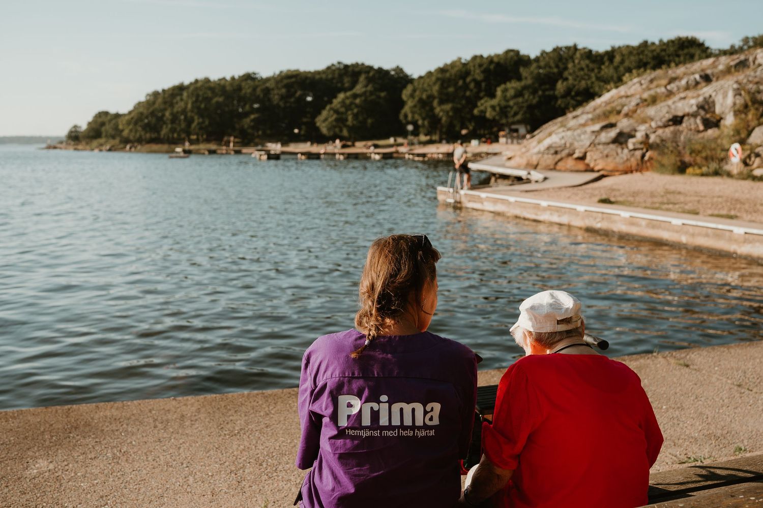 A caregiver and client sit together enjoying the view of a rocky coastline.