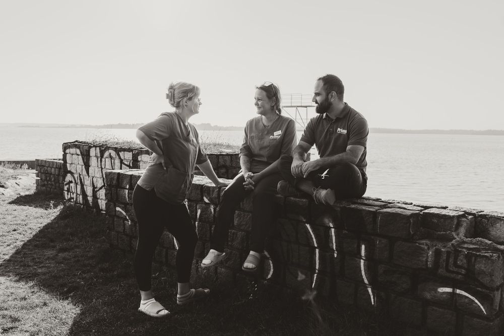 Three people engaged in conversation while sitting on rocky shoreline at sunset.