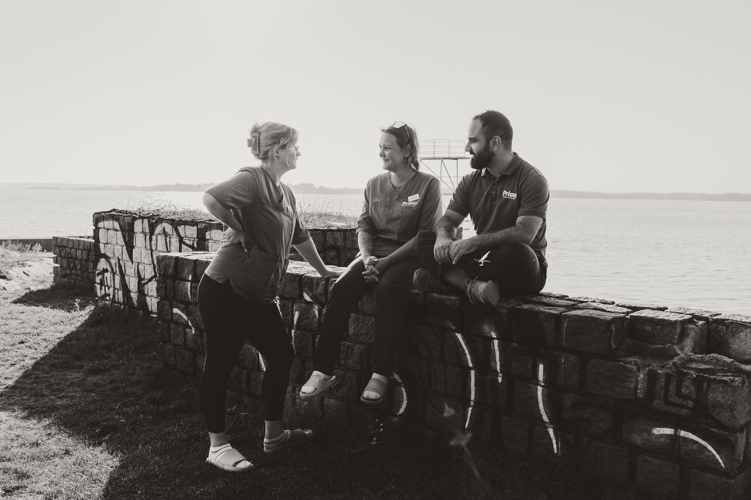 Three people engaged in conversation while sitting on rocky shoreline at sunset.