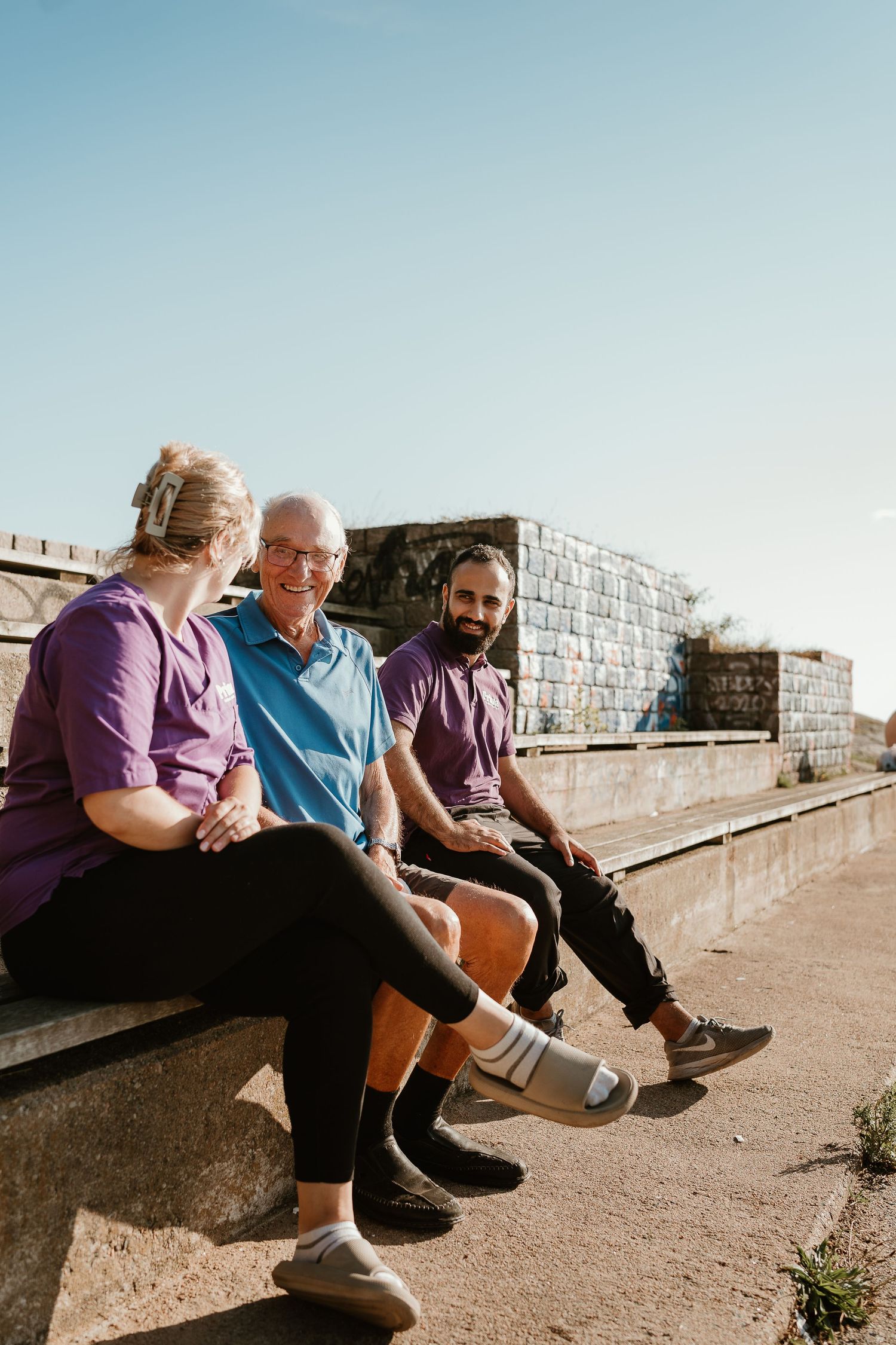 Three people sit together on a bench enjoying conversation on a sunny day.