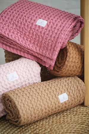 Stacked waffle-textured blankets in pink, cream and tan colors with small white tags.
