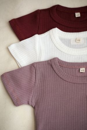 Three ribbed t-shirts laid flat in burgundy, white, and mauve colors.